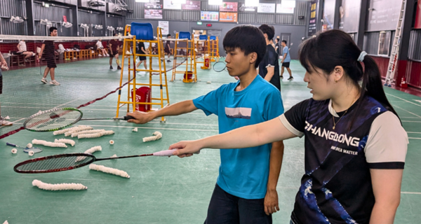 羽球教練示範正確羽球握拍動作，學生在一旁模仿與練習。