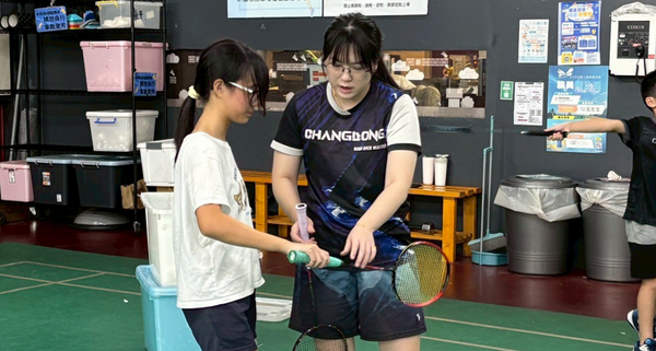 小朋友在寒假育樂營中練習羽球，羽球教練耐心在旁協助。